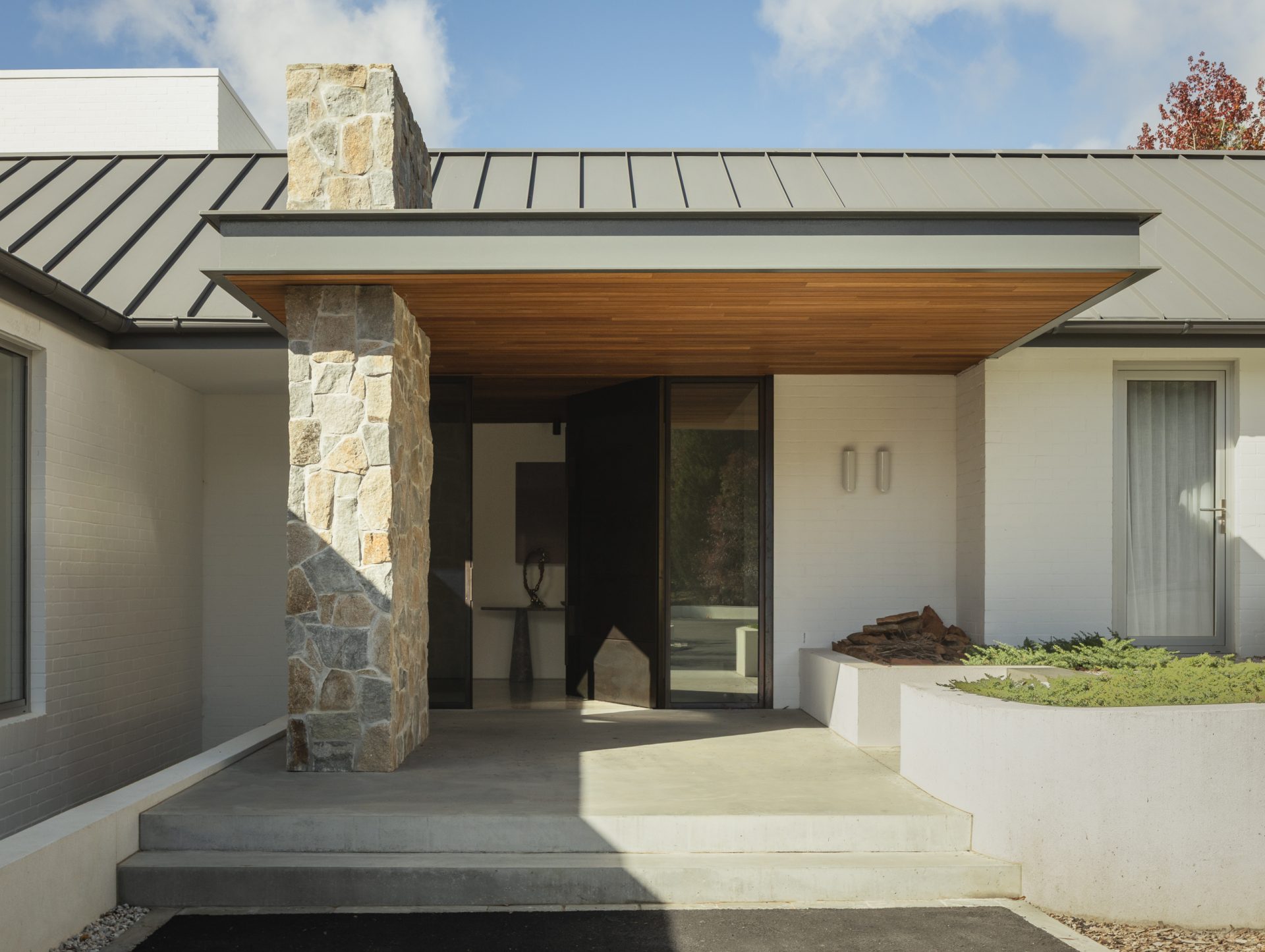 Stone-clad entry portico with pivoting bronze door at Melody House